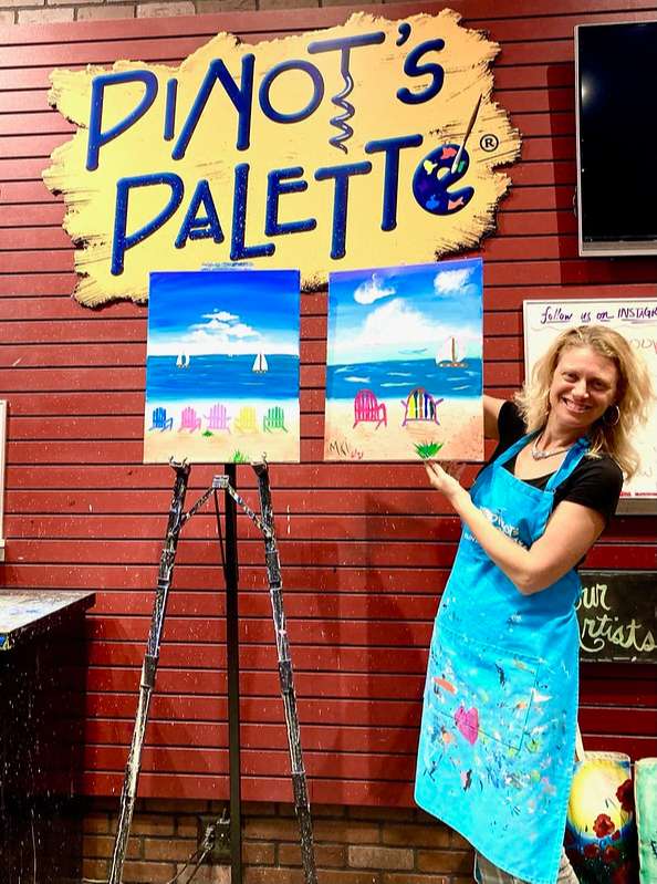 a blonde woman showing off her painting at pinot's palette