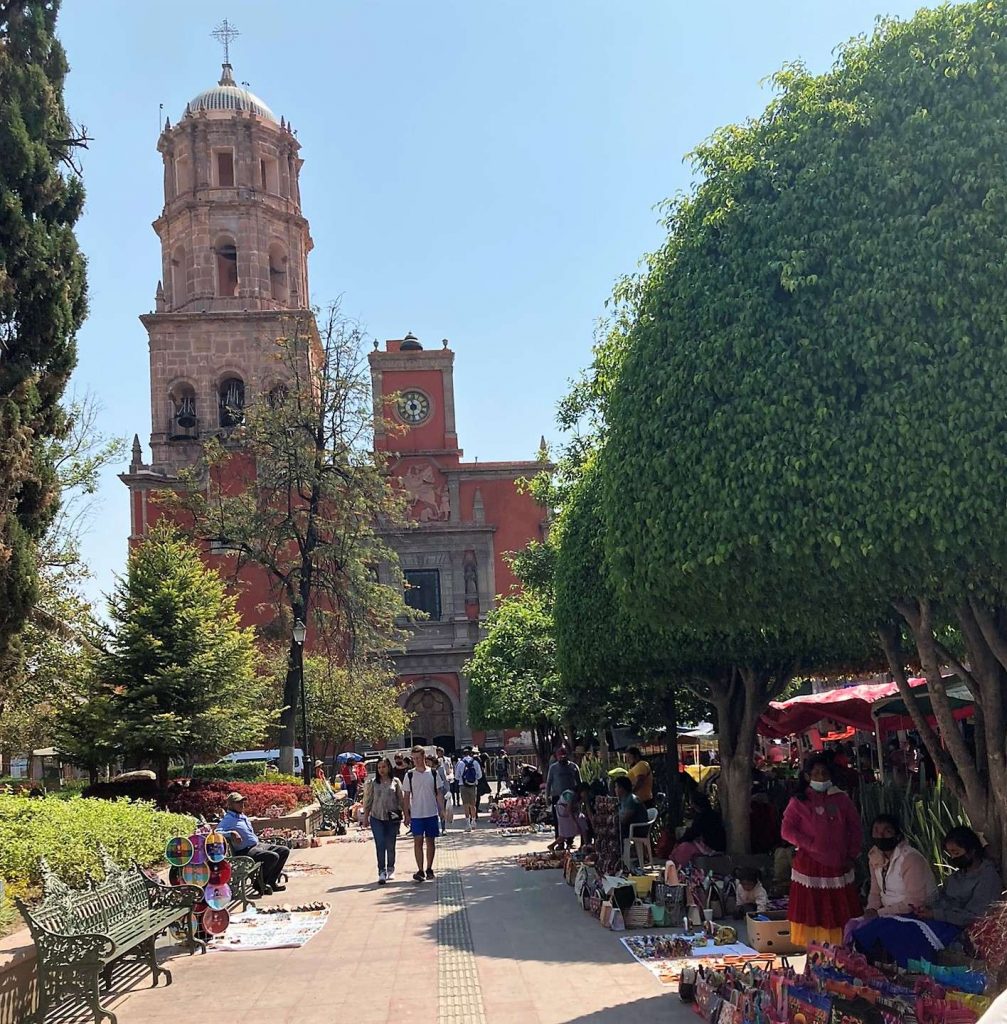 a street full of vendors and people walking with a old building on the back in queretaro