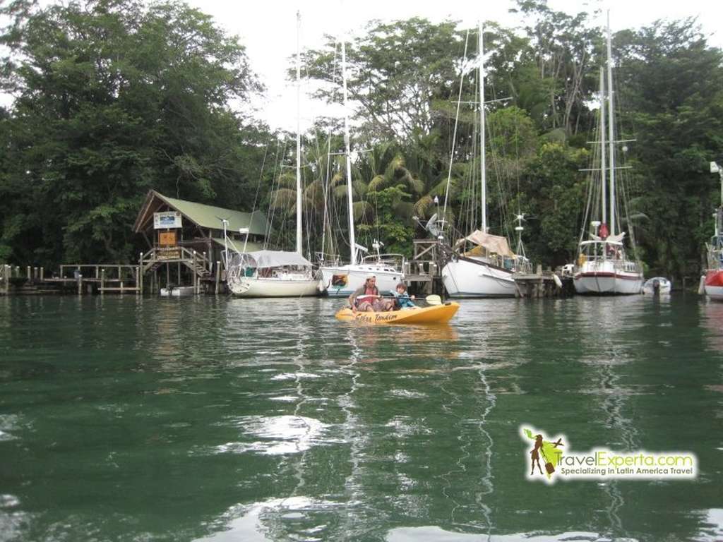 a kid and a man on a kayak in front of some boats in rio dulce guatemal